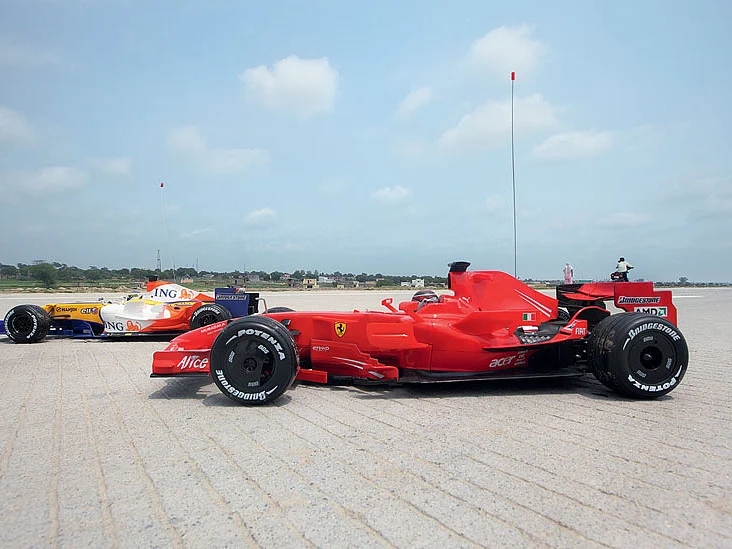 F1 car models against the backdrop of villages along the Yamuna Expressway.