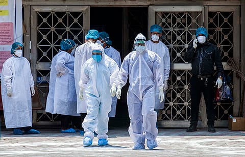 A group of healthcare workers in PPE kits outside a facility.